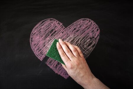 Hand removing chalk heart from black board