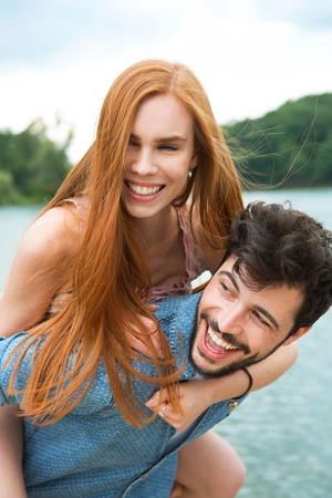 Happy couple at lake, man carrying girlfriend piggybackの写真素材