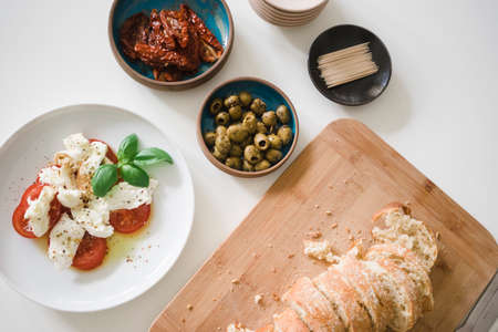Mozzarella and tomatos with basil, dried tomatoes and olives on turqouise plates, sliced breadの写真素材