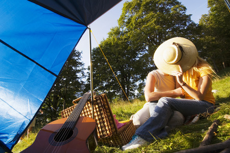 Young couple sitting in meadow, faces covered by hatの写真素材