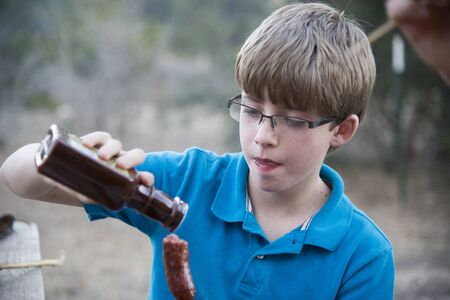 Young boy pouring barbecue sauce on grilled sausageの写真素材
