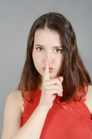 Young woman making hand gestures, finger on lipsの写真素材