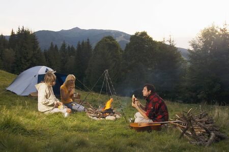 Three young poeple sitting around campfireの写真素材