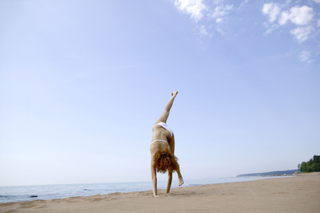 Young woman making handstand on beach