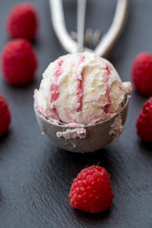 Raspberry-vanilla-icecream in icecream scoop, fresh raspberries on slate