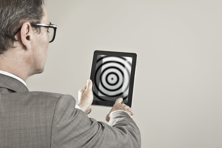 Close up of businessman looking at concentric screen of tablet pc against grey backgroundの写真素材