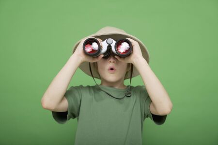 boy looking through binocular against green backgroundの写真素材