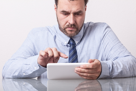 Business man on office desk, typing on tablet computer. Mature Caucasian/European adult, glass table with reflection.の写真素材
