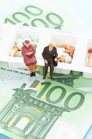 Figurines sitting on pill organizer with 100 euro notesの写真素材