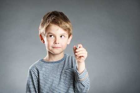 Portrait of boy with pen, thoughtful, grey backgroundの写真素材