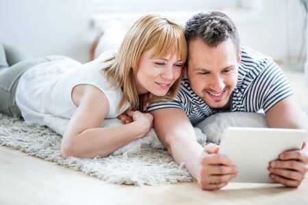 Couple with tablet lying on floor and surfing the netの写真素材