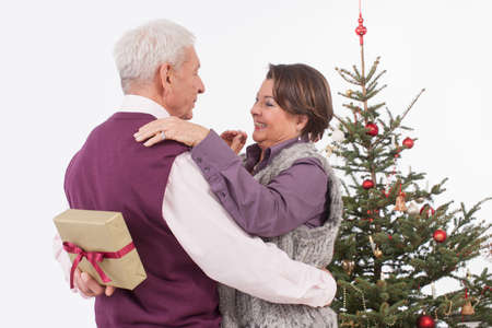Senior man hiding gift from senior woman at christmas, smilingの写真素材