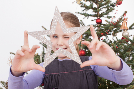 Girl winking through silver star shaped  smiling, portraitの写真素材
