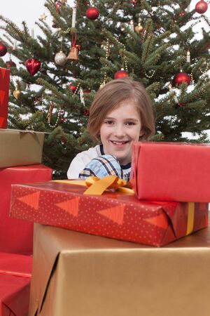 Boy sitting between Christmas gifts and tree, smiling, portraitの写真素材