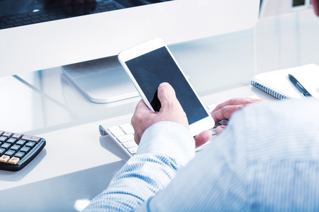 Anonymous business man typing on mobile device on office desk, view over the shoulder, glass table, computer keyboard.の写真素材