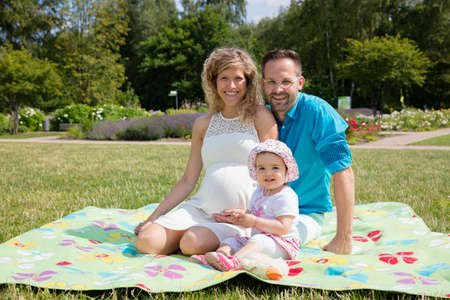 Happy couple expecting baby, sitting on blanket in parkの写真素材