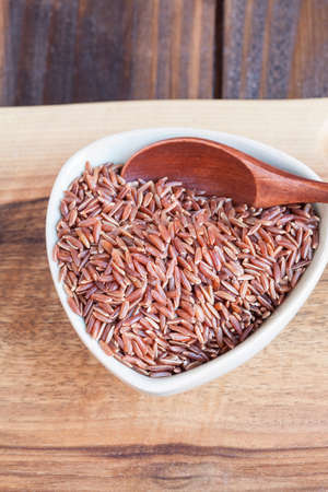 Red wholemeal rice in bowl, wooden spoonの写真素材