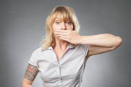 Young woman portrait on grey background, covering her mouthの写真素材