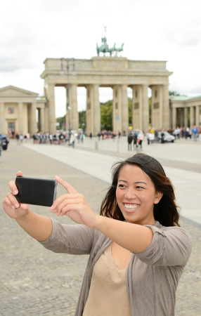Germany, young woman with smartphone in Berlin, selfie, Brandenburg Gateの写真素材
