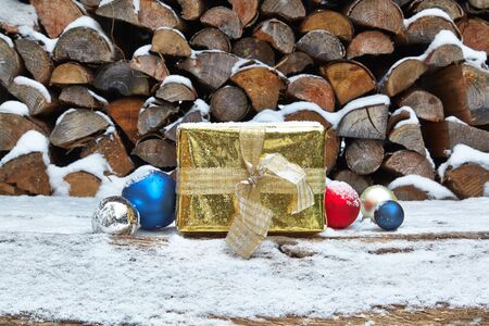 Golden christmas present and baubles in front of woodpileの写真素材