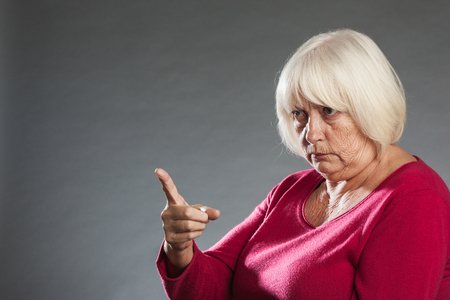 Female senior angrily pointing finger. Horizontal portrait on gray background with copy spaceの写真素材