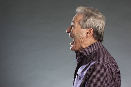 Profile view of male senior shouting. Horizontal portrait on gray background with copy spaceの写真素材