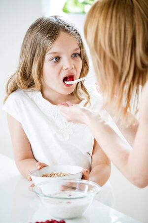 Mother feeding daughter with muesli and raspberriesの写真素材