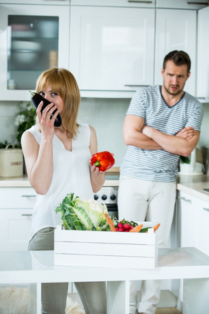 Woman with vegetable box in kitchen, man looking scepticalの写真素材