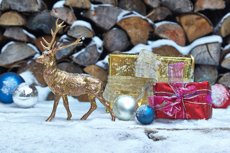 Christmas presents, baubles and deer figurine in front of woodpileの写真素材