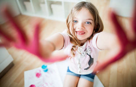 Young girl making pink hand prints on paperの写真素材