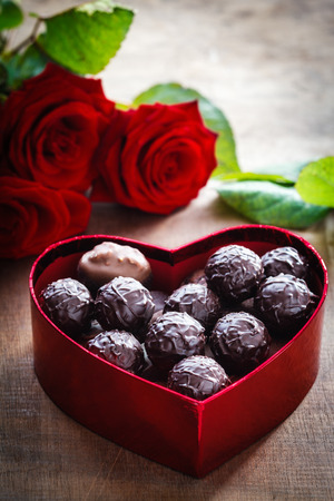 Chocolate truffles in heart shaped box and red roses on wood, valentine, mother's day presentの写真素材