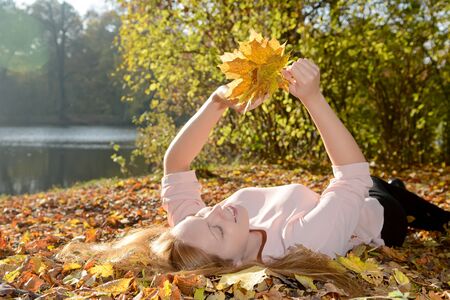Happy young woman lying on autumn leaves in park holding bunch of leavesの写真素材