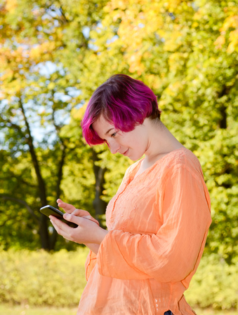 Young woman with smartphone in park, autumnの写真素材