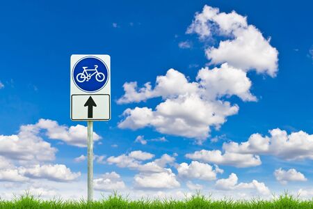 bicycle way sign on fresh spring green grass against blue skyの写真素材