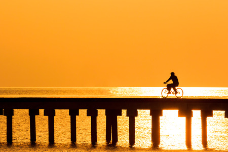 silhouette people driving bicycle  on wood bridge with sunsetの写真素材