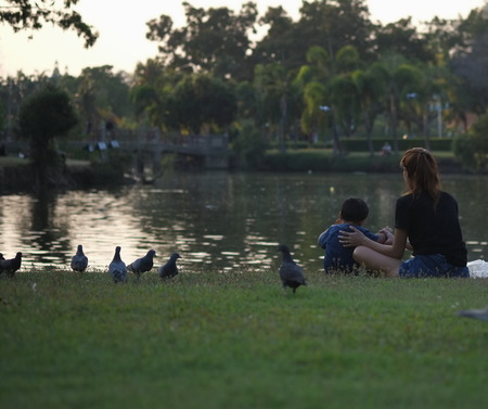 Mother and child sit and relax near the waterfront at the park in the evening.の写真素材