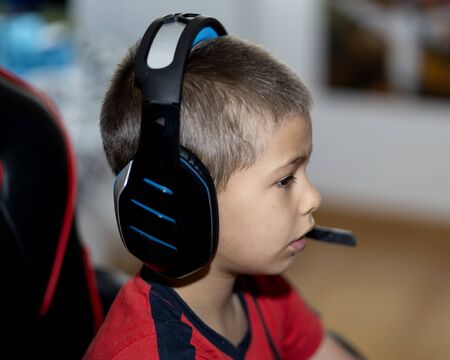 A boy playing a game console with headphones at homeの写真素材