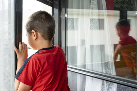 boy looking out the window towards the streetの写真素材