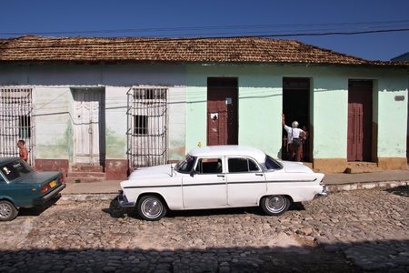 TRINIDAD, CUBA - FEBRUARY 5, 2011: People walk by oldtimer American "yank tank" car in Trinidad. Cuba has one of the lowest car-per-capita rates (38 per 1000 people in 2008).のeditorial素材