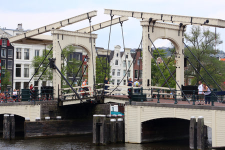 AMSTERDAM, NETHERLANDS - JULY 8, 2017: People visit Magere Brug (The Skinny Bridge) in Amsterdam,...