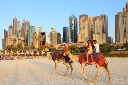 DUBAI, UAE - NOVEMBER 23, 2017: People ride camels in front of Jumeirah Beach Residence in Dubai, United Arab Emirates. Dubai has 14.9 million annual tourists.のeditorial素材