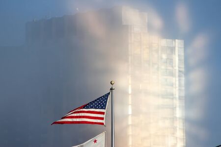 US flag - national symbol of the United States. San Francisco skyscraper in the clouds in background.の写真素材