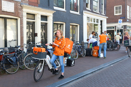 AMSTERDAM, NETHERLANDS - JULY 9, 2017: Uber Eats, Thuisbezorgd and Deliveroo food couriers wait in Amsterdam, Netherlands. Bicycle food delivery is popular in Amsterdam.のeditorial素材