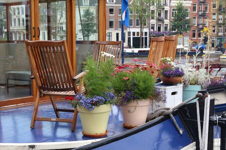 Amsterdam house boat deck with wooden chairs and flowers on Amstel river.の写真素材
