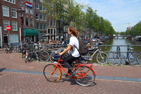AMSTERDAM, NETHERLANDS - JULY 10, 2017: Cyclist crosses Herengracht canal in Amsterdam, Netherlands. Amsterdam is the capital city of The Netherlands.のeditorial素材