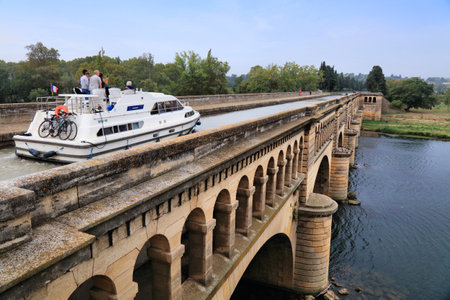 BEZIERS, FRANCE - OCTOBER 3, 2021: Boat across river Orb bridge on historic Canal du Midi in France. Canal du Midi is a UNESCO World Heritage Site.のeditorial素材