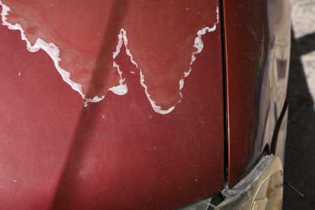 Weather damaged car hood paint coat. Peeling sun damaged paint surface in a 15 year old compact red car.の写真素材
