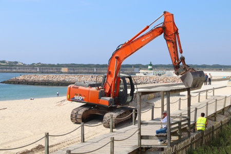 COSTA NOVA, PORTUGAL - MAY 23, 2018: Workers use Hitachi brand track excavator heavy machine to maintain beach sand erosion in Costa Nova, Portugal.のeditorial素材