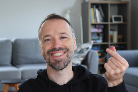 Man smiling and showing Asian or Korean style finger heart gesture. Bearded man wearing casual black...
