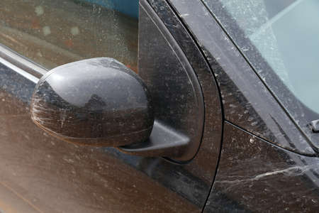 Dirty car needs a wash. Small black car with dirt on the body and side mirror.